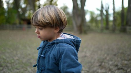 Foto de Triste niño pensativo camina hacia adelante fuera en el parque durante la temporada de otoño. Niño reflexivo en el aire libre sensación de preocupación - Imagen libre de derechos