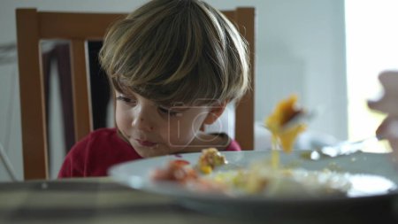 Photo for Relentless small boy at lunch table being fed food by parent, close-up of kid eating scrambled eggs during morning breakfast - Royalty Free Image