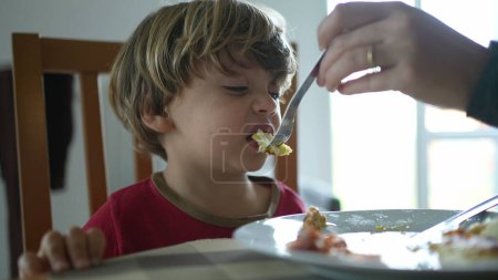 Téléchargez les photos : Alimentation des petits garçons en œufs brouillés pendant l'heure du déjeuner ou du petit déjeuner, gros plan de l'enfant nourri par les parents pendant la scène de style de vie fmaily - en image libre de droit