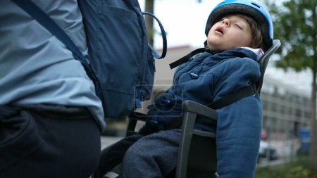 Photo for Child Asleep in Bicycle Backseat, Wearing Helmet during Ride. Little boy napping outside - Royalty Free Image