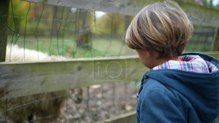 Photo for Little boy interacting with animal at farm, child pointing at goat in orgnanic agriculture farmland wearing jacket during autumn fall season - Royalty Free Image