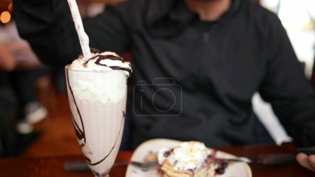 Téléchargez les photos : Homme appréciant les crêpes et milk-shake, savourer un dessert sucré au restaurant - en image libre de droit