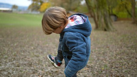 Photo for Little boy lifting feet checking dirty shoes outside at park during autumn fall season. Kid stepping in poop - Royalty Free Image