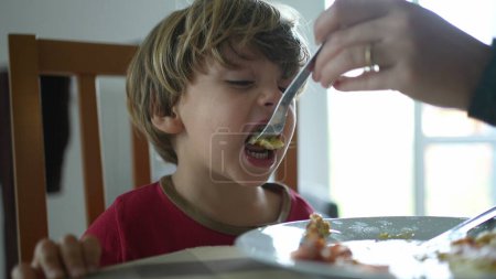 Téléchargez les photos : Alimentation des petits garçons en œufs brouillés pendant l'heure du déjeuner ou du petit déjeuner, gros plan de l'enfant nourri par les parents pendant la scène de style de vie fmaily - en image libre de droit