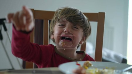 Photo for Small boy having a tantrum at lunch table. close-up face of child hitting table and crying displeased and with messy mouth - Royalty Free Image