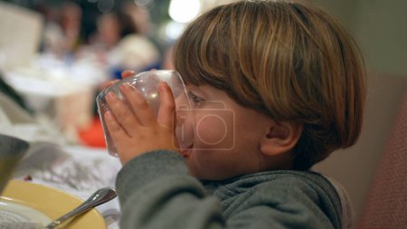 Photo for Closeup child drinking glass of water at restaurant. kid refreshing himself after meal, hydration concept - Royalty Free Image