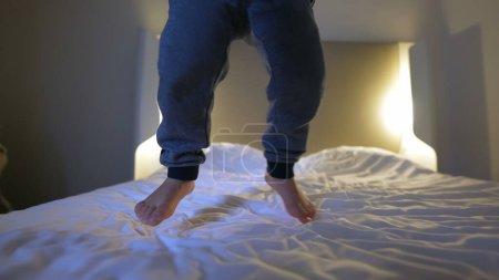 Téléchargez les photos : Joyeux garçon de 3 ans rebondissant sur le lit de l'hôtel - Plaisir de Voyage - en image libre de droit