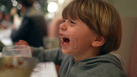 Foto de Feliz niño riendo, perfil de primer plano cara de la auténtica vida real del niño pequeño risa y sonrisa en el restaurante - Imagen libre de derechos