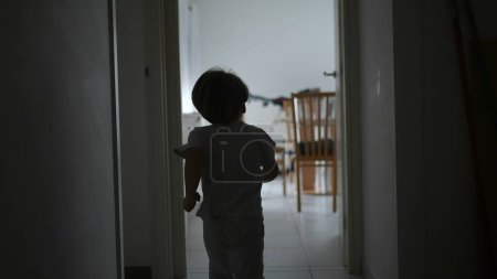 Foto de Detrás del niño corriendo en el pasillo del apartamento en cámara lenta. Un chico joven divirtiéndose en casa, silueta de ensueño de niño corriendo - Imagen libre de derechos