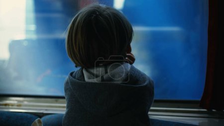 Téléchargez les photos : Derrière l'enfant réfléchi appuyé sur la fenêtre du train regardant le train parallèle sur le chemin de fer passer à grande vitesse. Enfant voyageant en rêvant - en image libre de droit