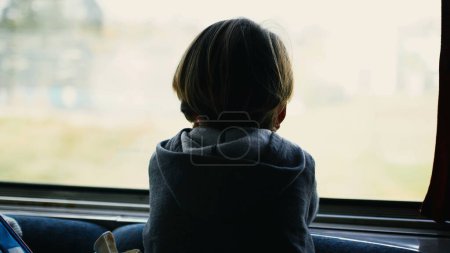 Foto de Atrás de un niño reflexivo apoyado en la ventana del tren mirando el tren paralelo en el ferrocarril pasan a alta velocidad. Niño viajando mientras soñaba despierto - Imagen libre de derechos