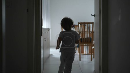 Foto de Detrás del niño corriendo en el pasillo del apartamento en cámara lenta. Un chico joven divirtiéndose en casa, silueta de ensueño de niño corriendo - Imagen libre de derechos