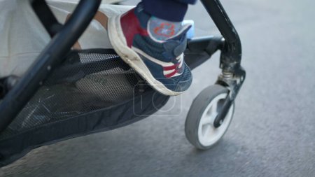 Photo for Stroller in Motion - Pushing Baby Carriage on Asphalt Sidewalk. Child's feet hanging outside while strolling in city - Royalty Free Image