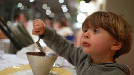 Photo for Child grabbing spoon and eating ice-cream dessert at restaurant, Small boy enjoying sugar food at night after dinner - Royalty Free Image