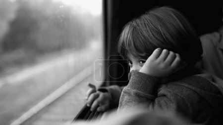 Foto de Pequeño niño mirando el paisaje pasar desde el asiento del tren en monocromático. Escena en blanco y negro de niños viajando y soñando despierto - Imagen libre de derechos