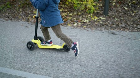 Téléchargez les photos : Gros plan enfants pieds équitation scooter à trois roues à l'extérieur - en image libre de droit