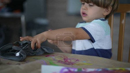 Foto de Pincel de mano infantil enjuague con agua y secado con toalla durante la sesión de pintura artística creativa en casa - Imagen libre de derechos