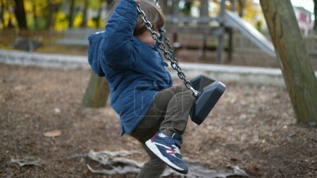 Photo for Child attempts to sit at park swing outside wearing blue jacket during autumn day - childhood trial and error concept - Royalty Free Image