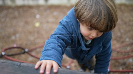 Photo for Happy active child climbing playground ropes during fall season. Autumn day play of 3 year old boy having fun outdoors, wearing blue jacket showing physical effort - Royalty Free Image