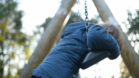 Photo for Playful Little Boy Twisting and turning while leaning on Park Swing during autumn fall park season. Carefree child engaged in play - Royalty Free Image