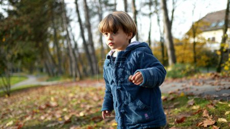Photo for Contemplative child standing at park with blue jacket amidst orange leaves during autumn fall season. Pensive thoughtful 3 year old boy in nature - Royalty Free Image