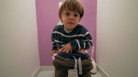 Téléchargez les photos : Enfant pensif assis aux toilettes de la salle de bain. Garçon de 3 ans faisant ses besoins dans les toilettes - en image libre de droit