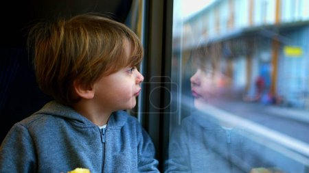 Foto de Un niño pequeño viajando en tren apoyado en el vidrio mirando fijamente, reflejo de la cara del niño en la ventana - Imagen libre de derechos