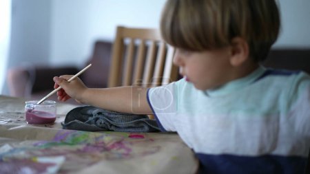 Foto de Pincel de enjuague infantil en casa mientras pinta, niño de 3 años comprometido con la sesión de trabajo de arte - Imagen libre de derechos