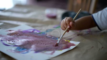 Photo for Closeup child hand holding paintbrush painting watercolor abstraction on paper, 3 year old kid engaged with artistic work at home - Royalty Free Image