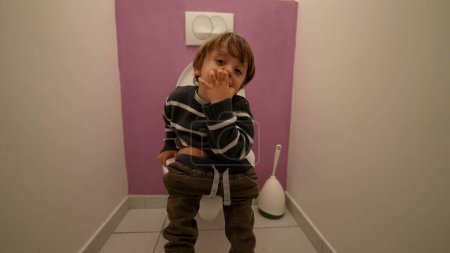 Téléchargez les photos : Petit garçon assis aux toilettes de la salle de bain et piquant du nez - en image libre de droit