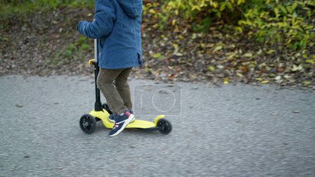 Photo for Closeup child feet riding three wheeled scooter outside - Royalty Free Image