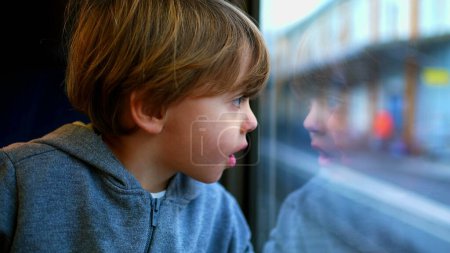 Photo for One small boy traveling by train leaning on glass staring at view, reflection of child's face on window - Royalty Free Image