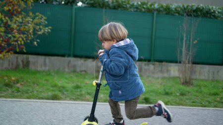 Téléchargez les photos : Garçon actif de trois ans jouissant d'une promenade en scooter à trois roues à l'extérieur - en image libre de droit