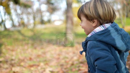 Téléchargez les photos : Joyeux enfant courant au parc pendant la saison automnale d'automne. Jeune garçon excité de 3 ans explorant la nature tout en portant une veste bleue, au milieu de feuilles orange - en image libre de droit