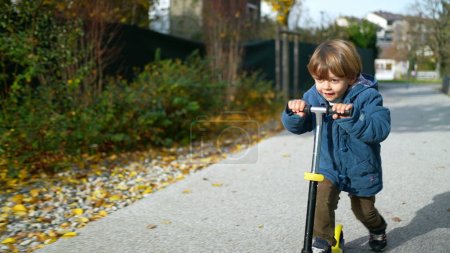 Photo for Joyful Three-Year-Old Boy Riding Toy Scooter Outdoors in Autumn Sunshine - Royalty Free Image
