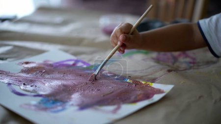 Téléchargez les photos : Gros plan enfant main tenant peinture au pinceau aquarelle abstraction sur papier, enfant de 3 ans engagé dans le travail artistique à la maison - en image libre de droit