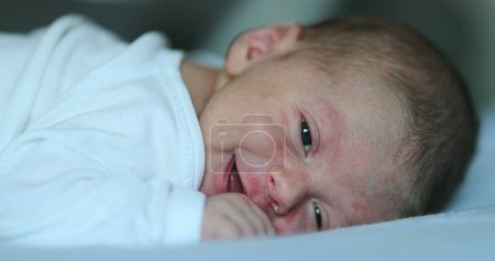Téléchargez les photos : Cute happy newborn baby smiling feedling joy, infant first week of life in bed - en image libre de droit