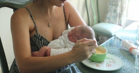 Téléchargez les photos : Mother eating food while holding newborn baby - en image libre de droit