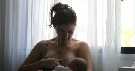 Foto de Mother breastfeeding newborn baby next to window - Imagen libre de derechos