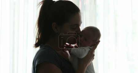 Foto de Mother kissing newborn baby infant next to window curtain - Imagen libre de derechos