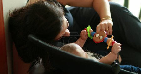 Foto de Candid mamá interactuando con el bebé recién nacido jugando con juguete en silla - Imagen libre de derechos