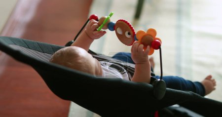 Téléchargez les photos : Cute baby playing with spinning toy infant seated in chair - en image libre de droit