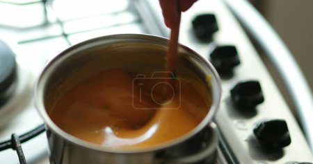 Téléchargez les photos : Gros plan de la main en remuant la soupe d'orange - en image libre de droit