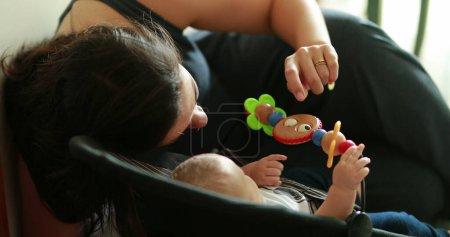 Foto de Candid mamá interactuando con el bebé recién nacido jugando con juguete en silla - Imagen libre de derechos