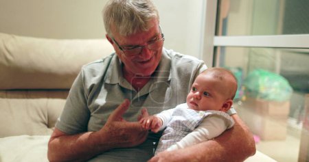 Téléchargez les photos : Grand-père tenant bébé petit-fils dans les bras moment familial authentique décontracté - en image libre de droit