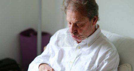 Téléchargez les photos : Older man holding and looking at cellphone device at home sofa - en image libre de droit