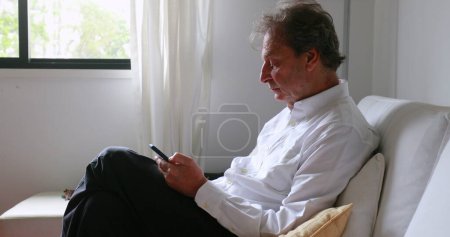 Photo for Older man looking at cellphone device at home sofa - Royalty Free Image
