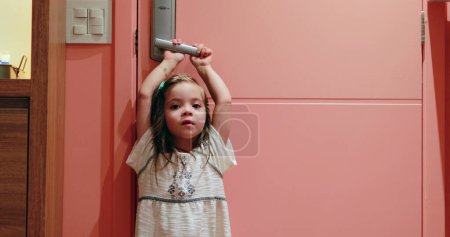 Téléchargez les photos : Bonne petite fille enfant tenant bouton de porte attendant et souriant - en image libre de droit