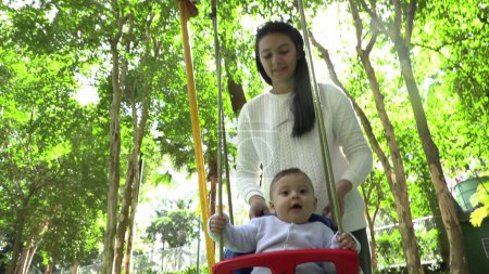 Téléchargez les photos : Bébé dans aire de jeux swing avec maman poussant - en image libre de droit