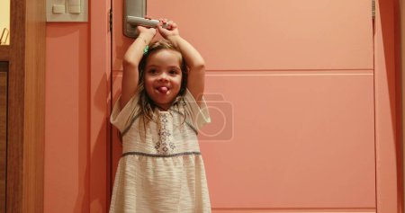 Foto de Small girl child holding door knob opening front door waiting for parent to arrive - Imagen libre de derechos